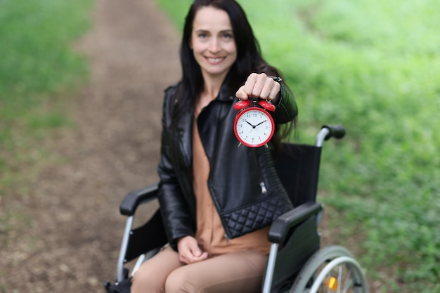 Mulher sorridente em cadeira de rodas segurando despertador no parque trabalho a tempo parcial para deficientes