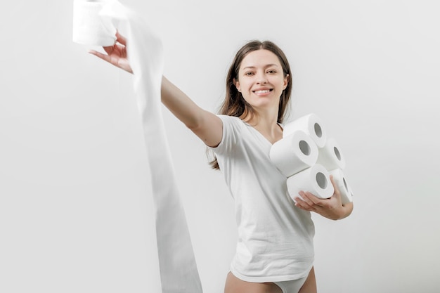 Mulher sorridente em camiseta branca segura rolos de papel higiênico nas mãos sobre fundo branco