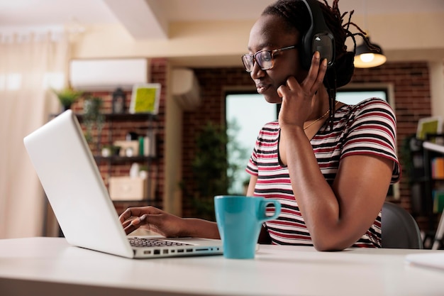 Mulher sorridente em fones de ouvido assistindo séries de tv online no laptop, freelancer tendo folga do trabalho. serviço de streaming, entretenimento doméstico, conceito de atividade de lazer de passatempo