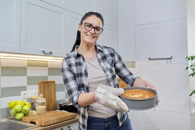 Mulher sorridente em luvas de cozinha com torta quente recém-assada