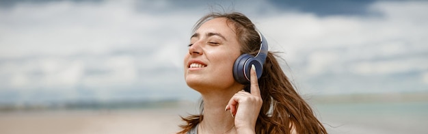 Mulher sorridente em roupas esportivas ouvindo música em fones de ouvido na praia no fundo do oceano