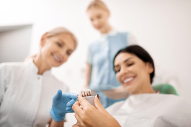 Mulher sorridente, escolhendo a cor para clarear os dentes, sentado na cadeira na clínica odontológica