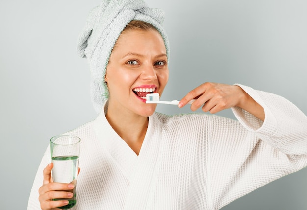Foto mulher sorridente escovando os dentes no banheiro de manhã menina feliz com escova de dentes e água de vidro