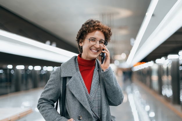 Mulher sorridente falando em um telefone celular em uma plataforma de metrô