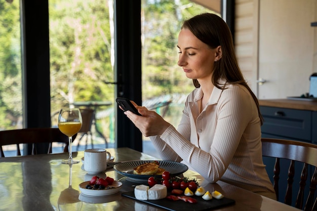 Mulher sorridente fazendo compras online no smartphone durante o almoço na cozinha