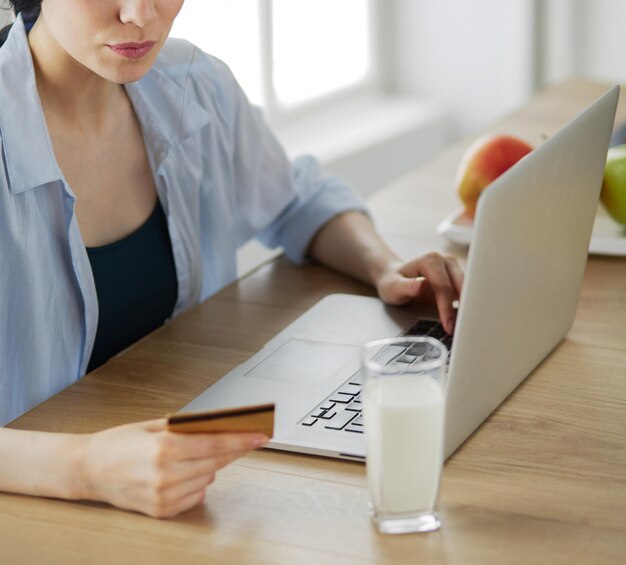 Mulher sorridente fazendo compras online usando computador e cartão de crédito na cozinha