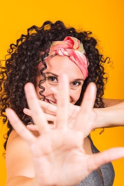 Foto mulher sorridente, fazendo mais cinco com as mãos sobre um fundo amarelo.