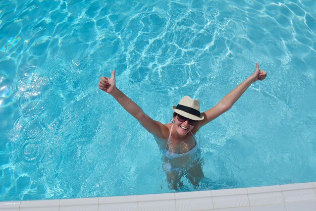 Mulher sorridente feliz com chapéu e óculos de sol na piscina no resort tropical