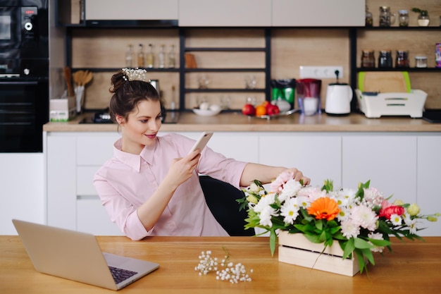 Mulher sorridente Florista Pequena empresa Proprietária de floricultura Ela está usando seu telefone e laptop para receber pedidos para sua loja online Tirar fotos