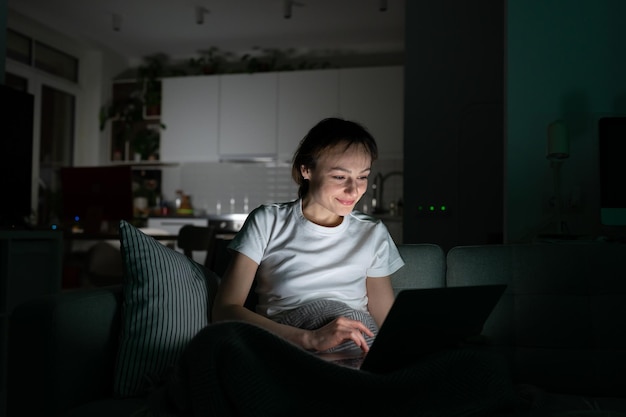 Mulher sorridente freelancer sentada no sofá trabalhando no laptop falando em videochamada à noite em casa