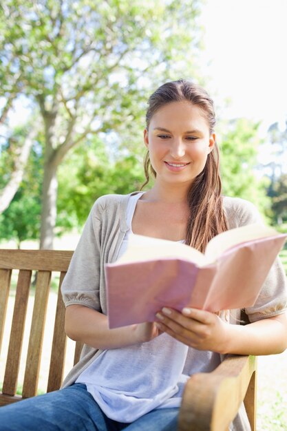 Mulher sorridente lendo seu livro em um banco de parque