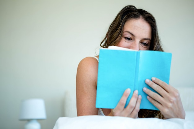 mulher sorridente, lendo um livro na cama