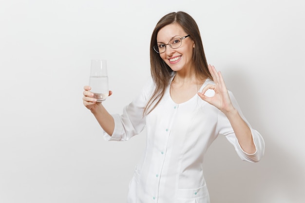 Mulher sorridente linda médica isolada no fundo branco. Médica em vestido branco de médico, óculos segurando um copo de água, mostrando o gesto de ok. Pessoal de saúde, saúde, conceito de medicina.