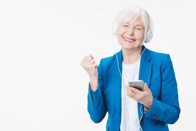 Mulher sorridente madura com fones de ouvido ouvindo música no telefone e dançando isolado