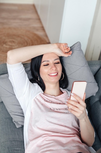 Foto mulher sorridente mentindo e usando o celular em casa