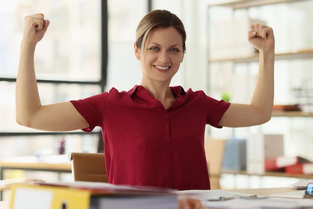 Mulher sorridente mostra músculos à mesa no escritório da empresa funcionária pronta para