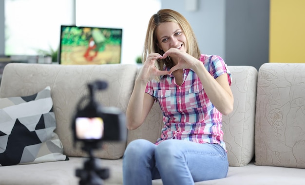 Foto mulher sorridente mostra seu coração para a câmera no tripé