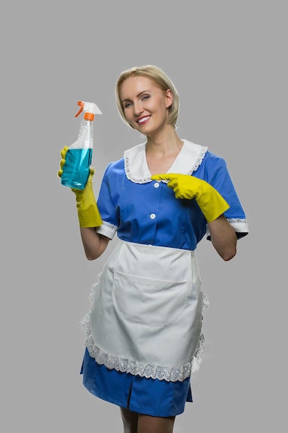 Mulher sorridente mostrando detergente para limpeza. Empregada doméstica bonita oferecendo spray de limpeza em fundo cinza. Serviço de limpeza da casa.