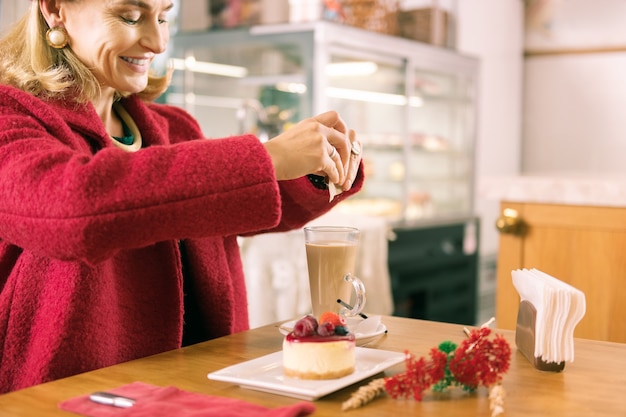 Mulher sorridente. Mulher madura sorridente e elegante com rugas faciais colocando açúcar no café