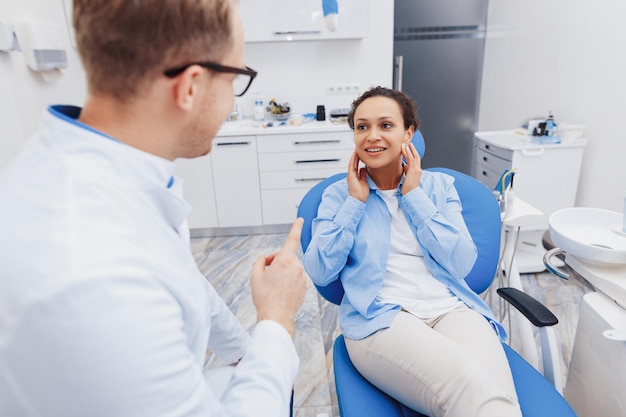 Mulher sorridente na cadeira odontológica conversando com o médico e mostrando dor de dente