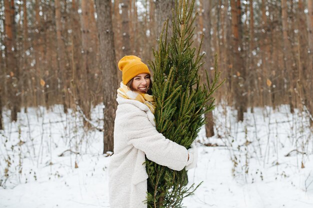 Mulher sorridente na floresta de inverno abraça a árvore de Natal. Vista lateral