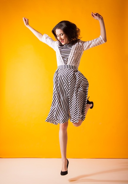 Mulher sorridente na moda em lindo vestido posando em movimento de estúdio atirou sobre amarelo