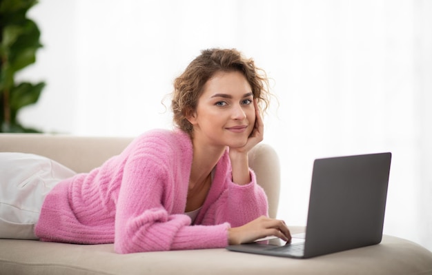 Mulher sorridente navegando na internet no laptop enquanto relaxa no sofá em casa