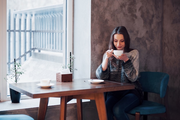 Mulher sorridente no café usando telefone celular e mensagens de texto em redes sociais, sentado sozinho