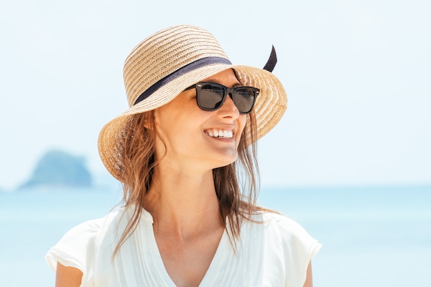 Mulher sorridente no vestido branco em pé na praia