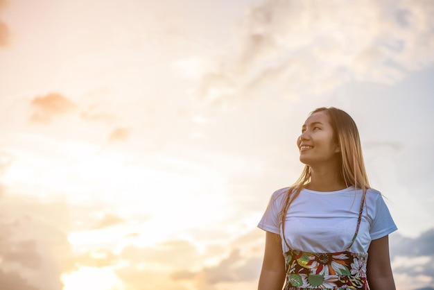 Foto mulher sorridente olhando para longe enquanto está de pé contra o céu durante o pôr do sol