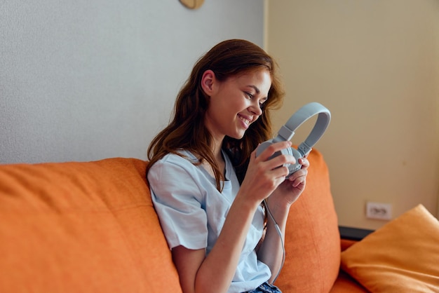 Mulher sorridente ouvindo música com fones de ouvido nas tecnologias de sofá laranja