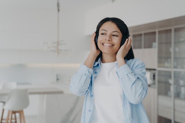 Mulher sorridente ouvindo música em fones de ouvido sem fio desfrutando de som musical descansando em casa