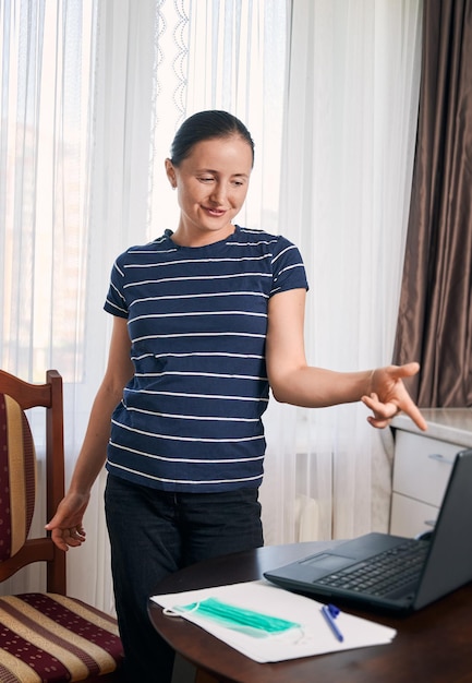 Mulher sorridente parada em seu local de trabalho em casa na frente de seu laptop se divertindo após um longo dia de trabalho Auto-isolamento durante o período de crise Fique em casa, salve o conceito de vidas