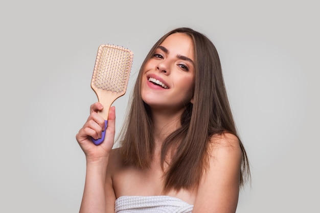 Mulher sorridente, penteando o cabelo com o pente. Linda garota penteando o cabelo comprido com a escova de cabelo