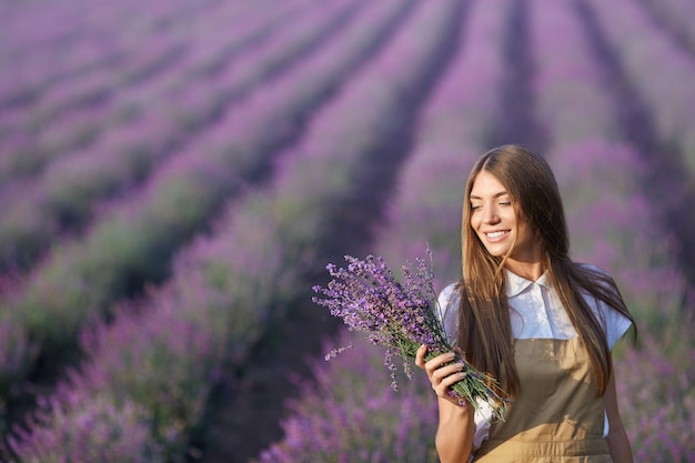 Mulher sorridente posando com buquê em campo de lavanda