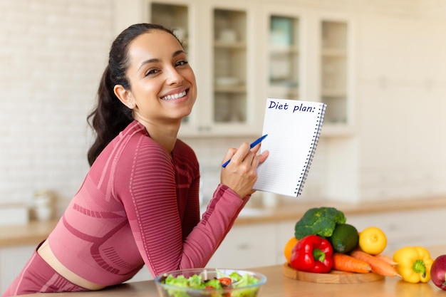 Foto mulher sorridente posando com plano de dieta na cozinha moderna