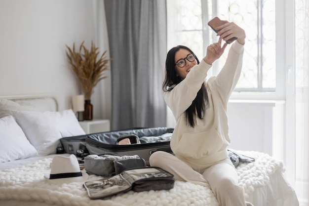 Mulher sorridente, posando na cama, tirando uma selfie com bagagem, viagem de verão, viagens de férias no quarto