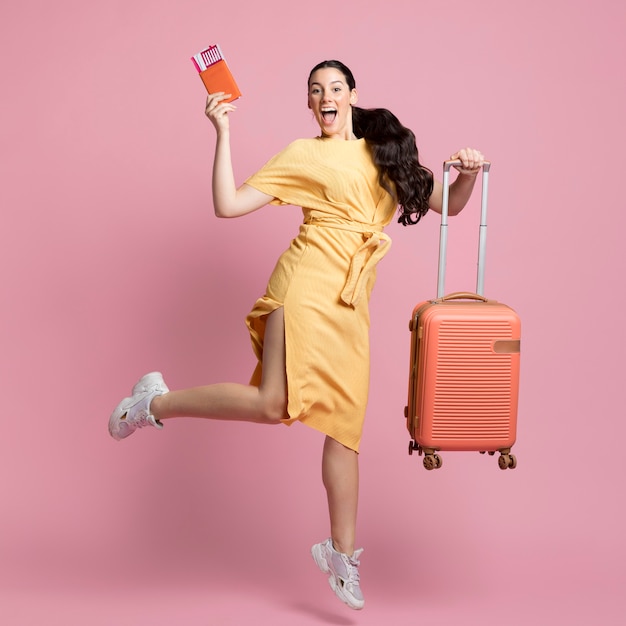 Mulher sorridente pulando enquanto segura sua bagagem e passaporte
