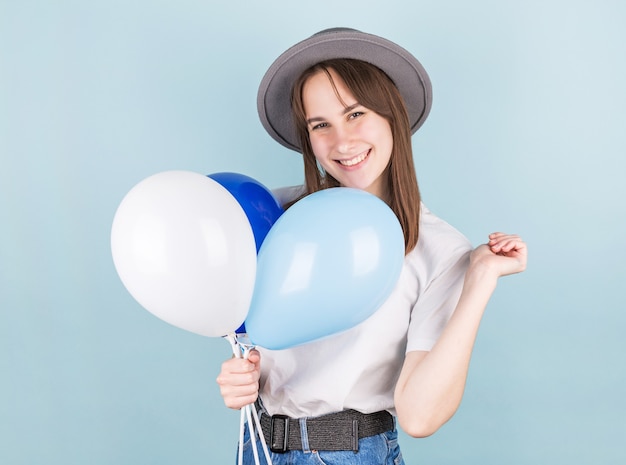 Mulher sorridente segurando balão e olhando para a câmera sobre fundo azul.