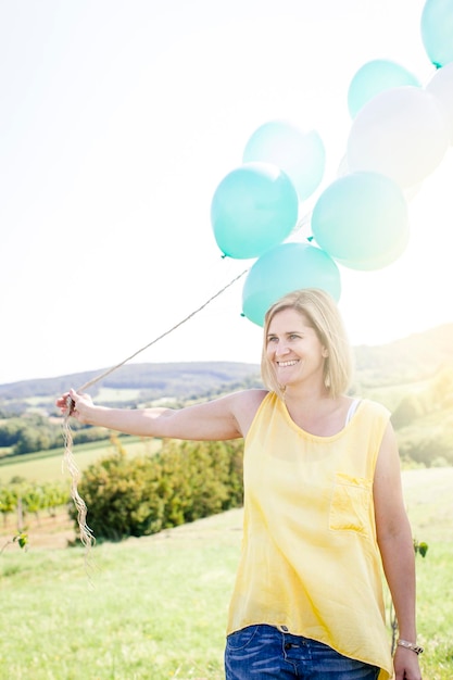 Foto mulher sorridente segurando balões contra o céu no campo