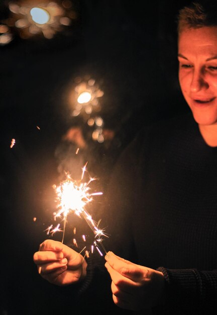 Foto mulher sorridente segurando faíscas iluminadas à noite