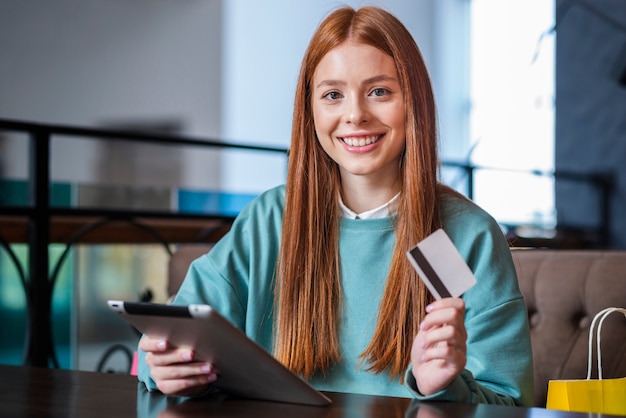 Mulher sorridente segurando o cartão de crédito e tablet