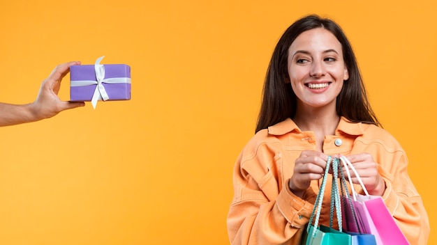 Foto mulher sorridente segurando sacolas de compras e olhando para o presente que ela ofereceu