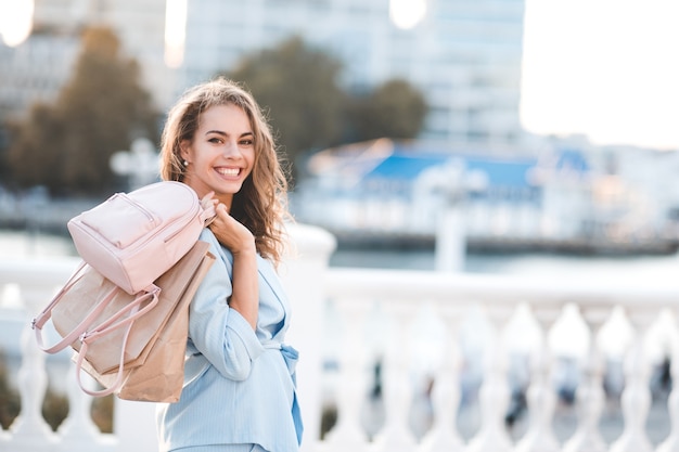 Mulher sorridente segurando sacolas de papel e mochila ao ar livre