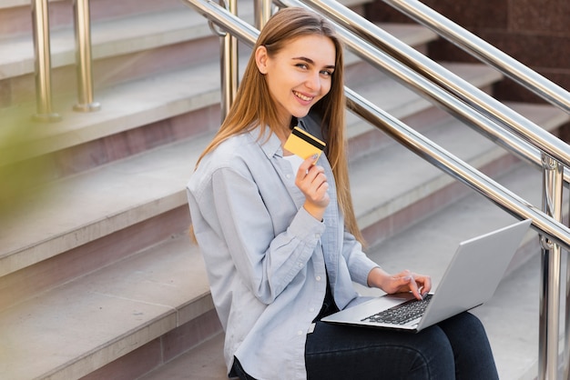 Mulher sorridente segurando um laptop e um cartão de crédito