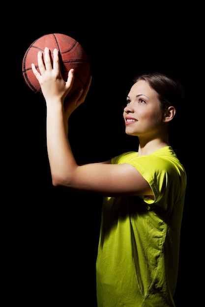 Mulher sorridente segurando uma bola enquanto olha para longe contra um fundo preto