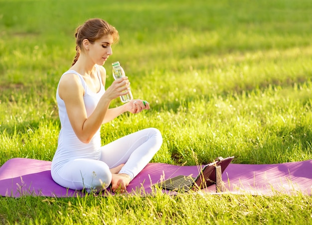 Mulher sorridente segurando uma garrafa esportiva de água na esteira de ioga no parque