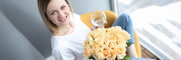 Mulher sorridente segurando uma taça de vinho e um buquê de flores nas mãos