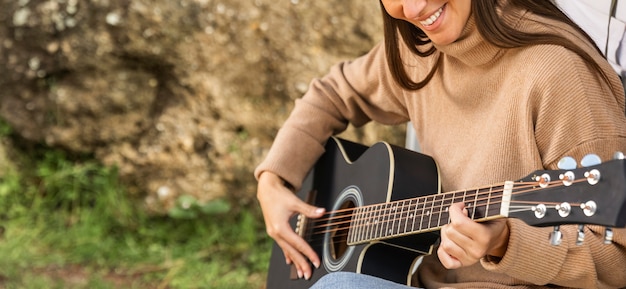 Foto mulher sorridente sentada no porta-malas do carro durante uma viagem e tocando violão