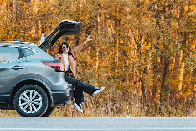 mulher sorridente sentada no porta-malas do carro parada para descanso na viagem